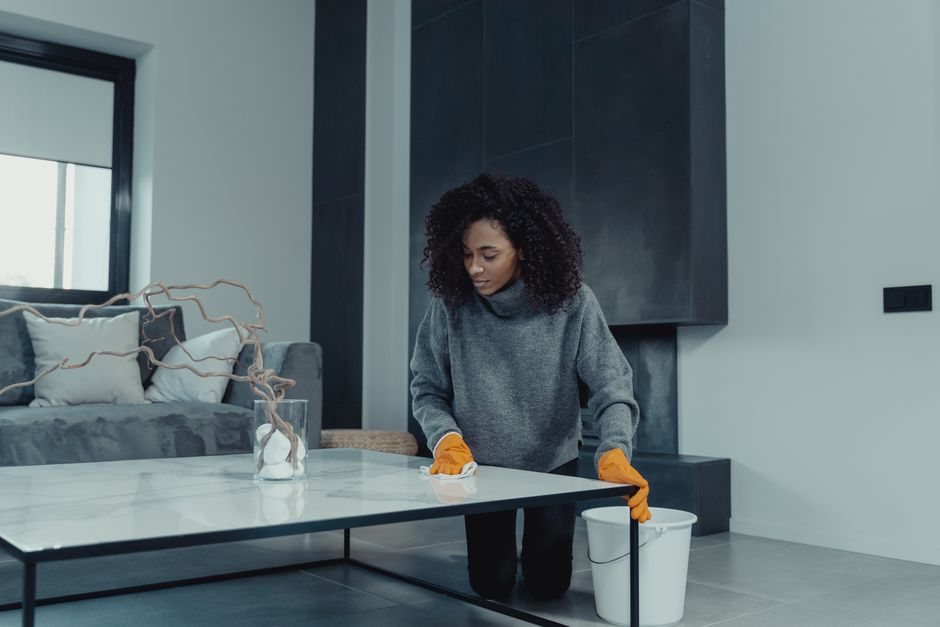 A woman wearing gloves cleans a table in a contemporary living room setting.