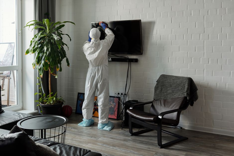 A person in protective gear meticulously cleans a television in a stylish living room.